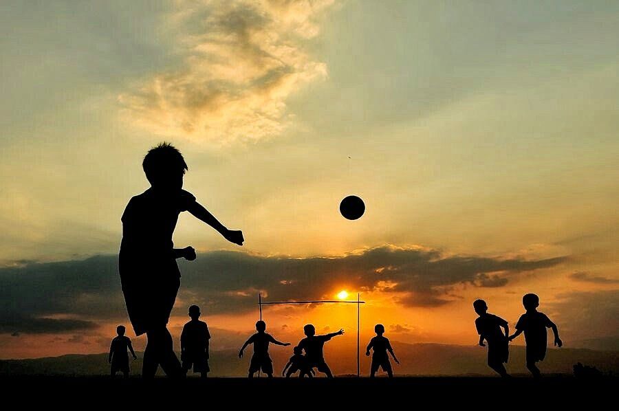 Chicos jugando al fútbol a contraluz en un atardecer
